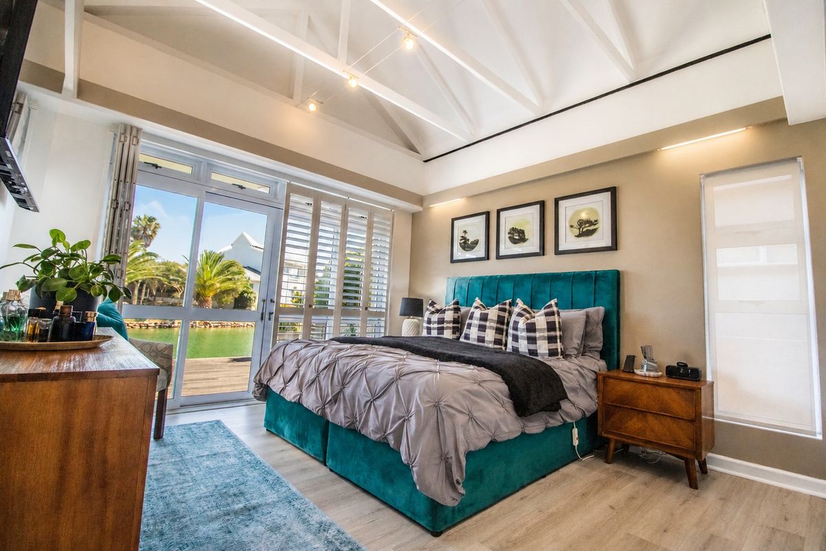 A well-appointed bedroom featuring vaulted ceilings with exposed rafters, laminate flooring, and sliding glass doors that open to a waterfront view.