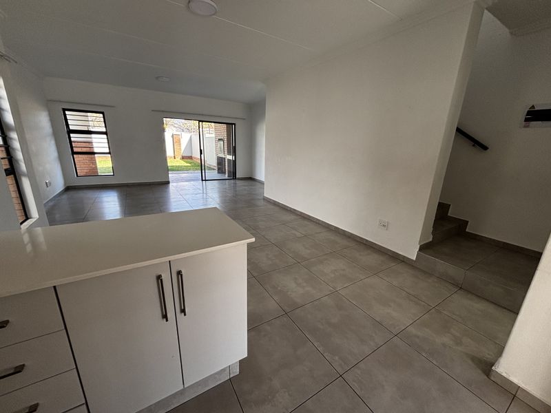 An open-plan living area featuring neutral tiled flooring, modern kitchen cabinetry, and direct access to the rear garden through sliding glass doors.