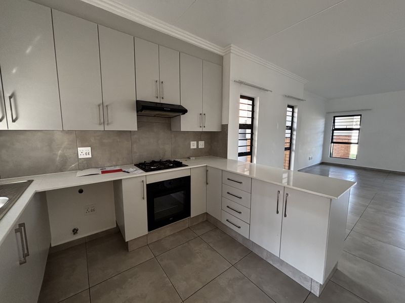 Modern open-plan kitchen featuring sleek cabinetry, stone countertops, integrated gas hob, and oven, flowing seamlessly into a bright, tiled living area.
