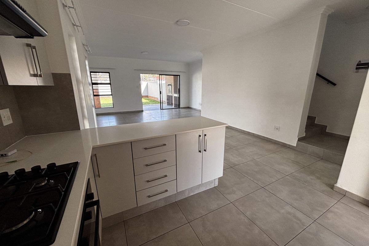 Open-plan kitchen and living area featuring modern cabinetry, gas hob, tiled flooring, and direct access to the rear patio through sliding glass doors.