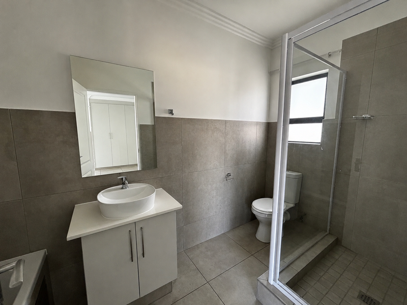 A modern, clean bathroom featuring a vessel sink vanity, a glass-enclosed shower, and neutral floor-to-ceiling tiling.