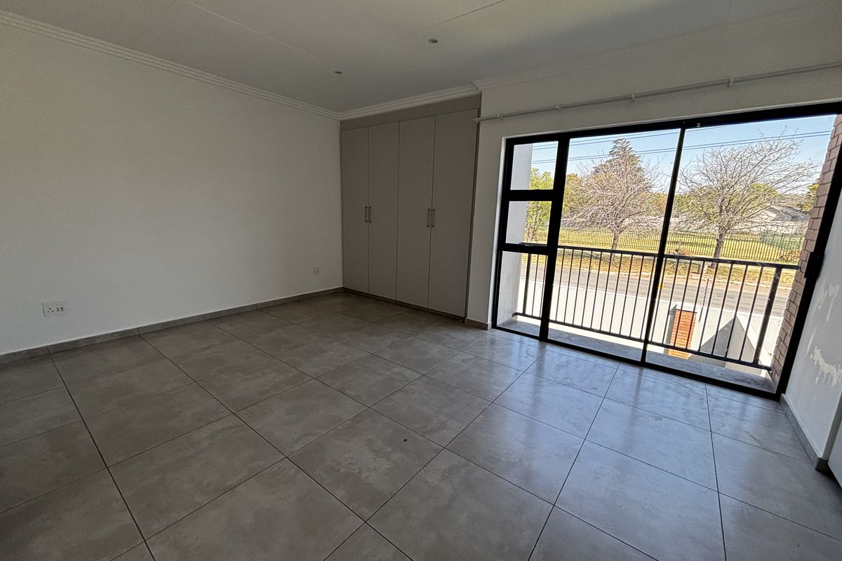 Spacious bedroom featuring neutral tiled flooring, built-in cupboards, and a large sliding glass door providing access to a balcony.