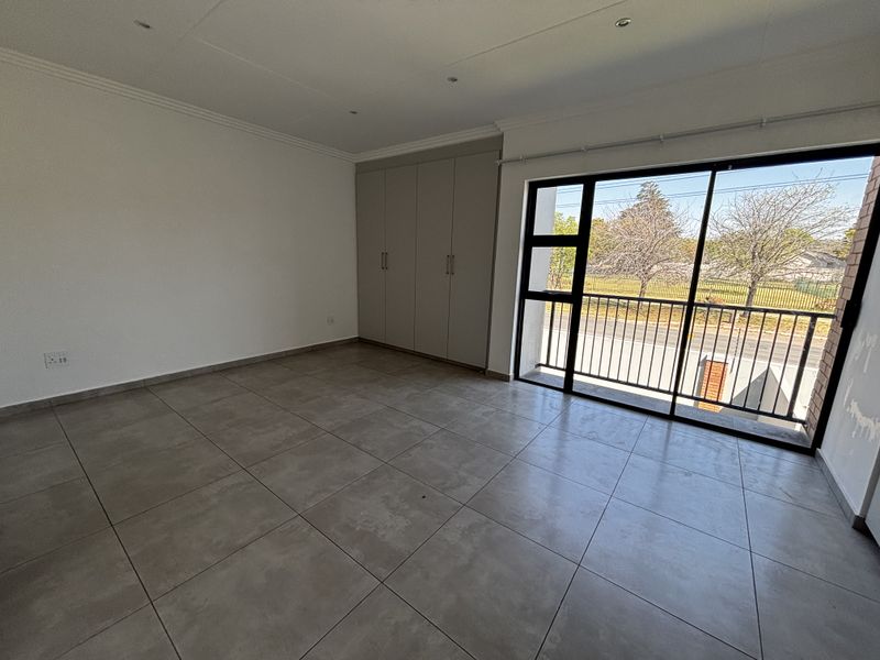 Spacious bedroom featuring neutral tiled flooring, built-in cupboards, and a large sliding glass door providing access to a balcony.