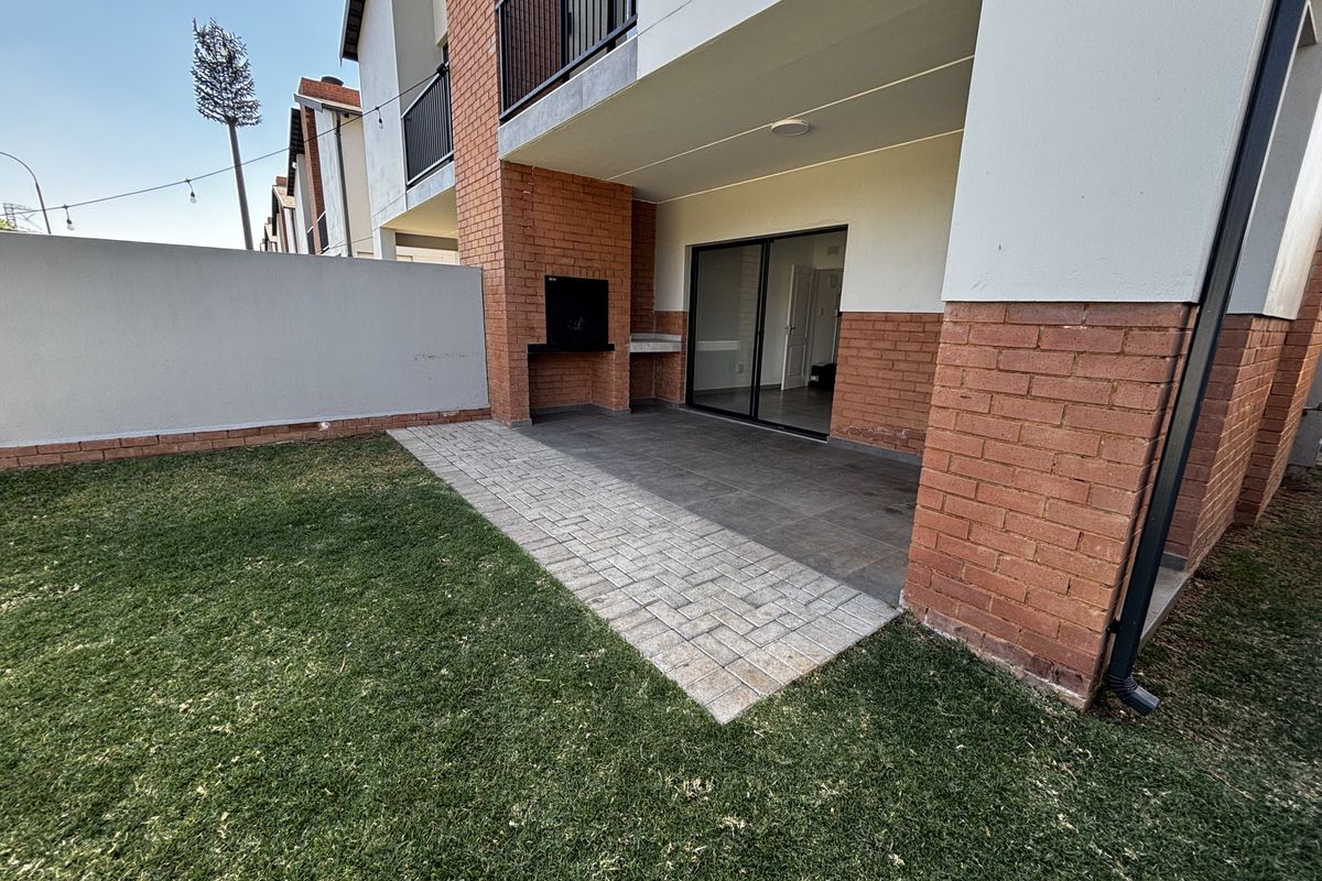 A private rear garden featuring a paved patio area with a built-in braai and direct access to the interior via sliding glass doors.