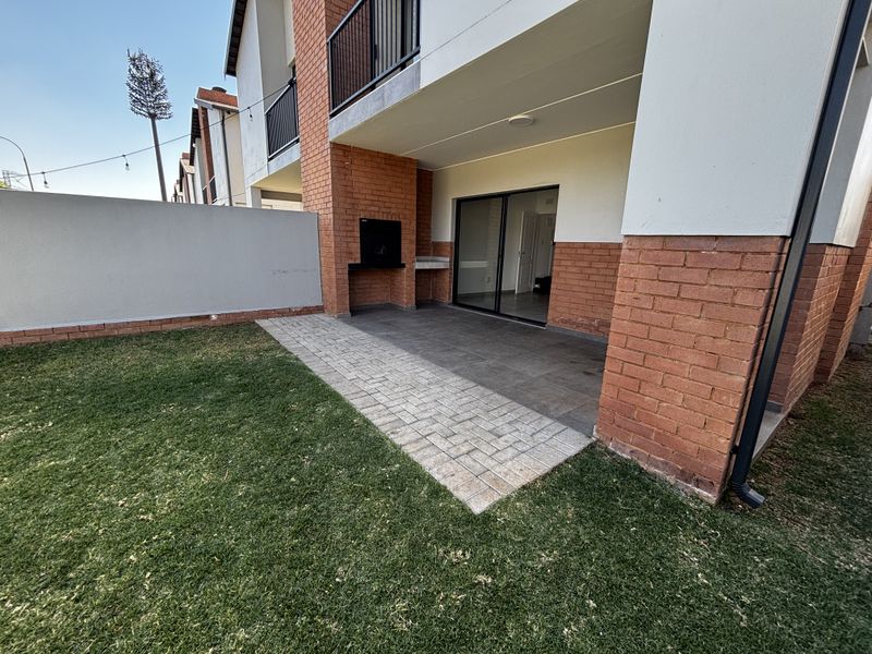 A private rear garden featuring a paved patio area with a built-in braai and direct access to the interior via sliding glass doors.