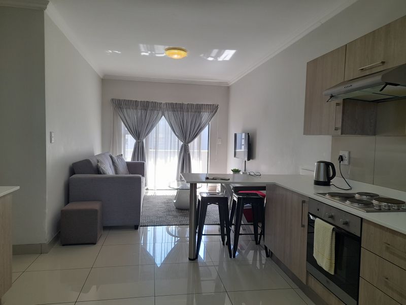 Open-plan living area featuring a modern kitchen with built-in appliances, breakfast bar, and tiled flooring, leading to a bright lounge with balcony access.