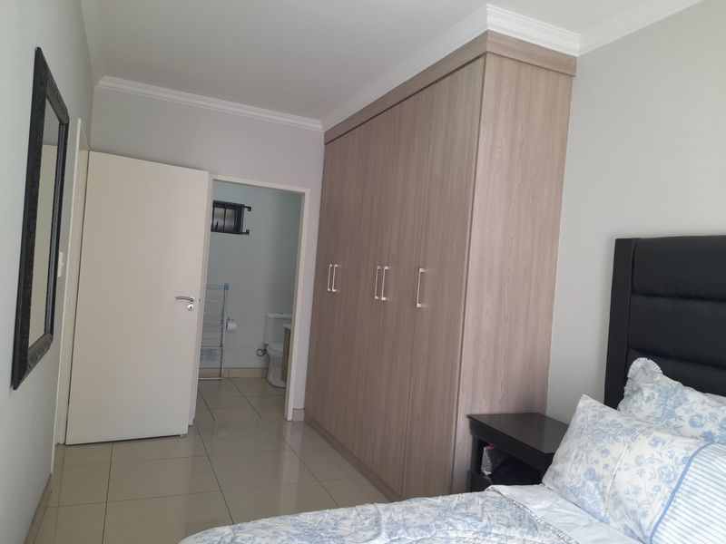A well-maintained bedroom featuring neutral tiled flooring, crown molding, and a large built-in wardrobe with wood-grain finish, providing direct access to an en-suite bathroom.