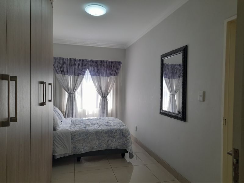 A well-maintained bedroom featuring built-in cupboards, neutral tiled flooring, and ample natural light through the window.