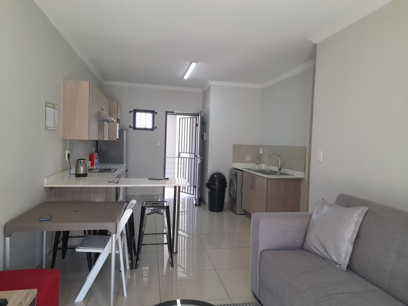 Open plan kitchen and living area featuring modern cabinetry, tiled flooring, and direct access to an exterior security gate.
