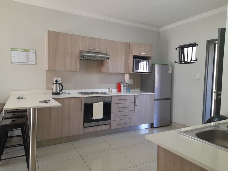Modern kitchen featuring light wood-finish cabinetry, integrated appliances including an oven and hob, a breakfast bar, and tiled flooring.
