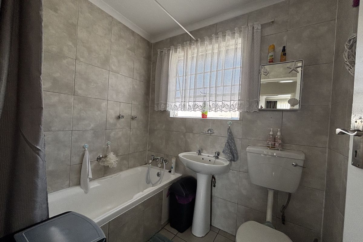 A functional bathroom featuring a bathtub, pedestal basin, and toilet with neutral wall and floor tiling.