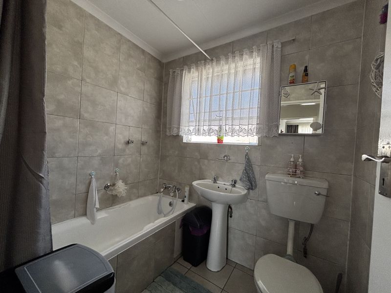 A functional bathroom featuring a bathtub, pedestal basin, and toilet with neutral wall and floor tiling.