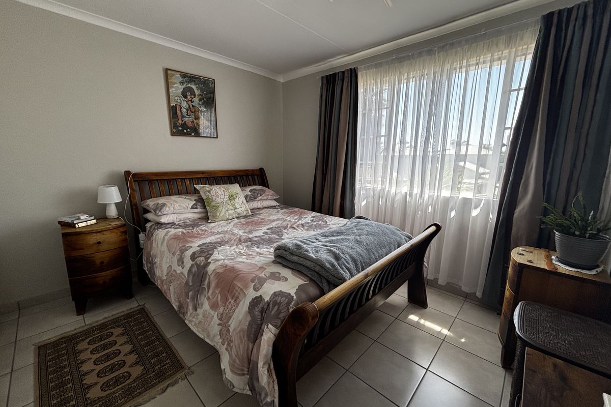 A well-lit bedroom featuring neutral wall tones, tiled flooring, and large windows with installed curtain tracks, offering a comfortable and functional living space.