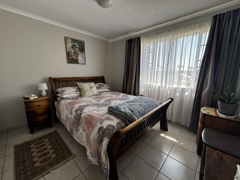 A well-lit bedroom featuring neutral wall tones, tiled flooring, and large windows with installed curtain tracks, offering a comfortable and functional living space.