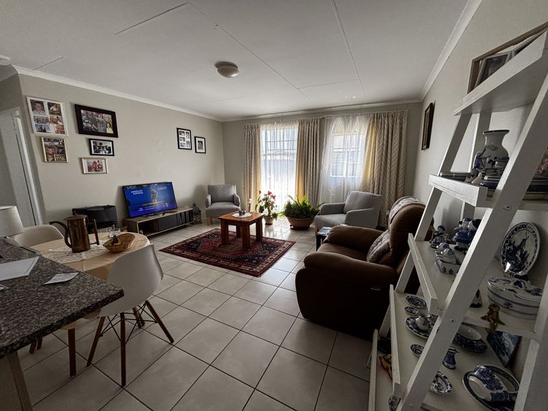 An open-plan living and dining area featuring neutral tiled flooring, ample natural light through window treatments, and a functional kitchen breakfast bar.