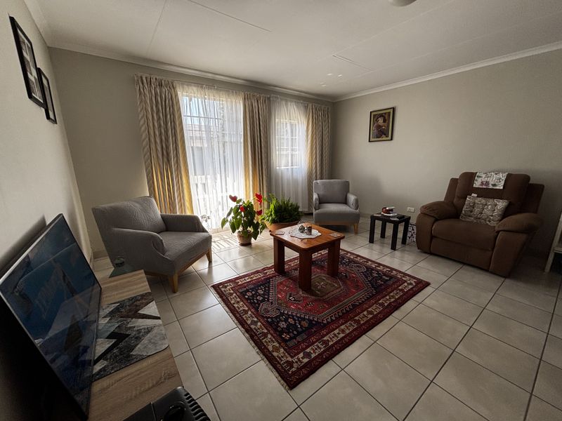 A well-lit living room featuring neutral tiled flooring, coved ceilings, and a sliding glass door providing access to the exterior.