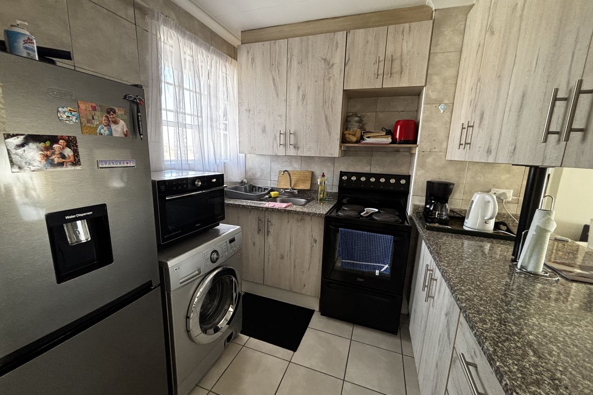 Compact kitchen featuring light wood-grain cabinetry, granite countertops, tiled backsplash, and integrated space for a washing machine and large refrigerator.