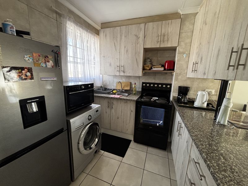 Compact kitchen featuring light wood-grain cabinetry, granite countertops, tiled backsplash, and integrated space for a washing machine and large refrigerator.