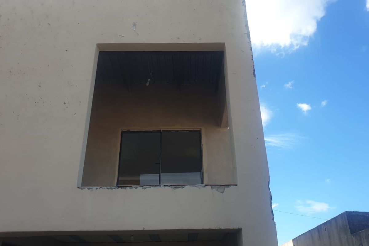Exterior view of a multi-story building featuring a balcony with a sliding glass door and visible signs of unfinished plasterwork and exterior wear.