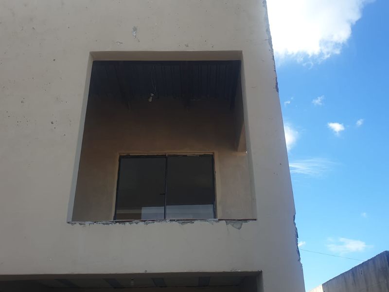 Exterior view of a multi-story building featuring a balcony with a sliding glass door and visible signs of unfinished plasterwork and exterior wear.