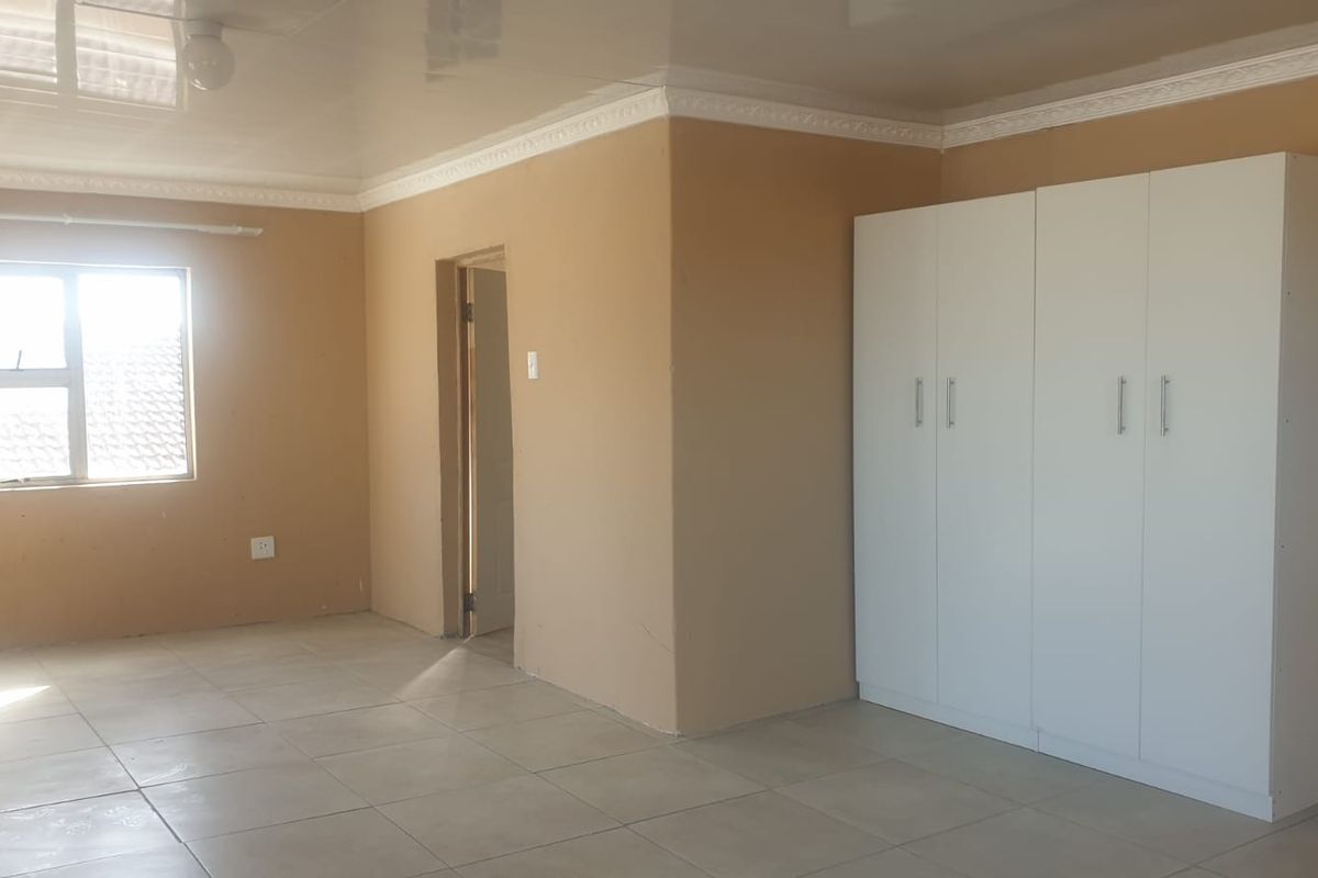 A spacious, empty bedroom featuring neutral wall tones, tiled flooring, a glossy ceiling with decorative cornice, and a large white built-in wardrobe.
