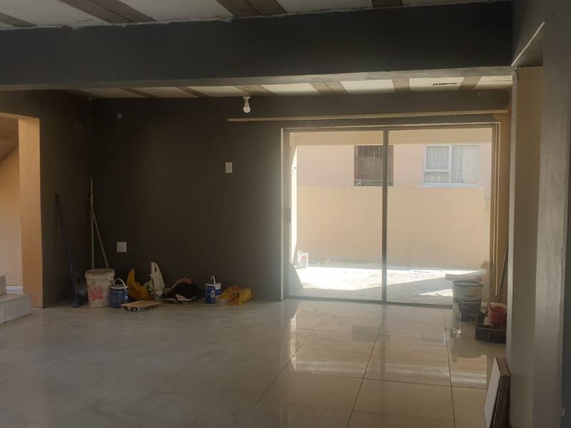 An unfinished open-plan living area featuring tiled floors, exposed ceiling beams, and a sliding glass door leading to an outdoor space.