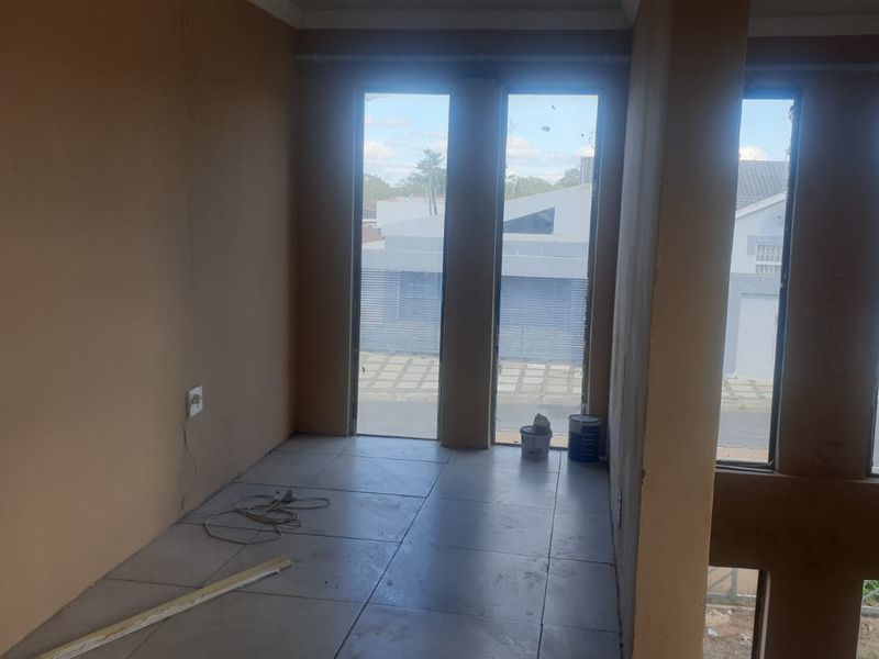 An empty, unfinished living area featuring large windows and tiled flooring, currently in a state of renovation.