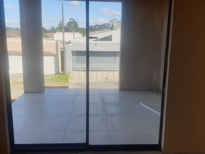 An unfinished covered patio area featuring tiled flooring and concrete support pillars, accessible via a sliding glass door.