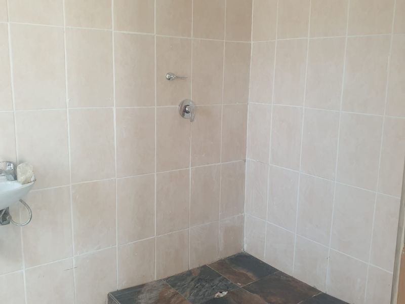 A basic bathroom featuring tiled walls and flooring, a wall-mounted basin, and a shower mixer, currently requiring maintenance and fixture updates.