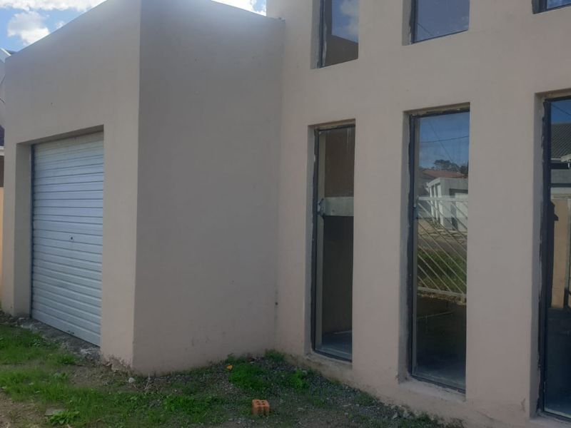 Front elevation of a modern house featuring a roller garage door and tall vertical windows with unfinished exterior detailing.