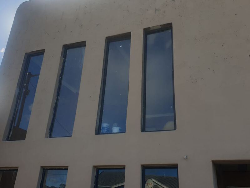 Exterior view of a building facade featuring multiple tall vertical windows and a stucco finish showing signs of wear and weathering.