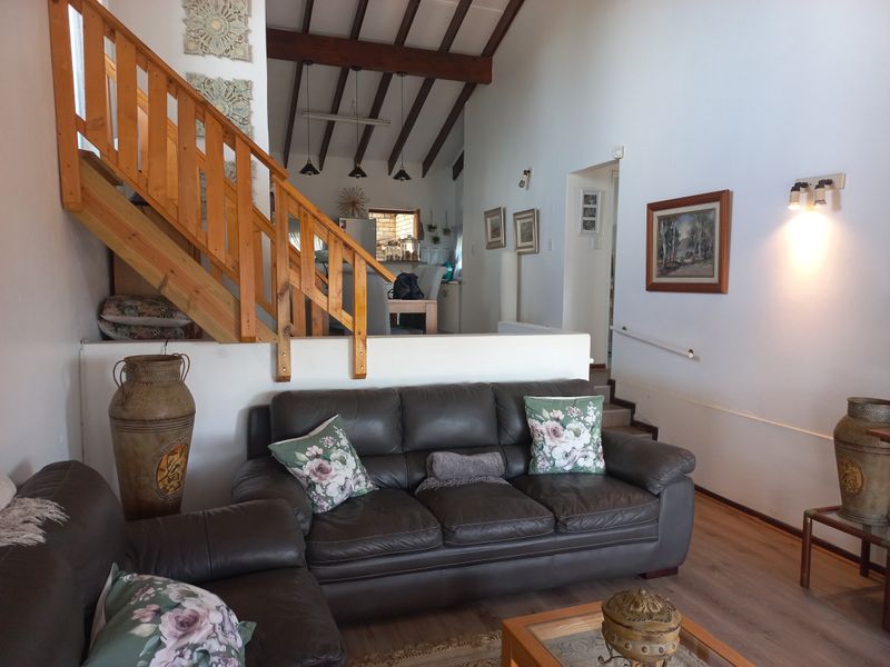 Open-plan living area featuring high vaulted ceilings with exposed timber beams, a wooden staircase, and laminate flooring, creating a spacious and rustic atmosphere.