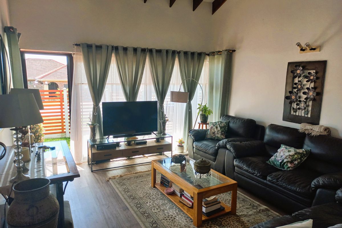 A comfortable living room featuring exposed timber ceiling beams, laminate flooring, and a sliding glass door providing access to the outdoor area.