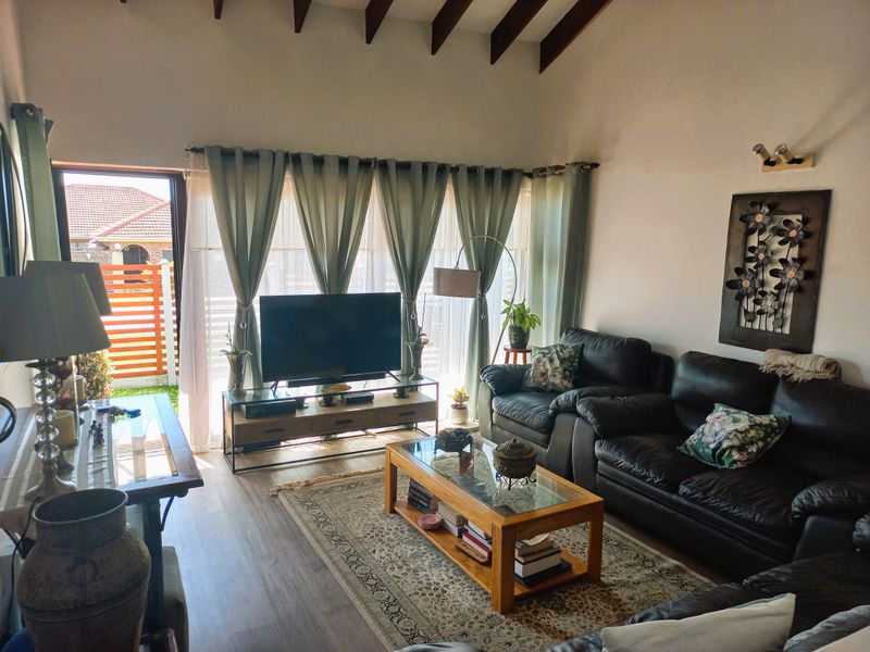 A comfortable living room featuring exposed timber ceiling beams, laminate flooring, and a sliding glass door providing access to the outdoor area.