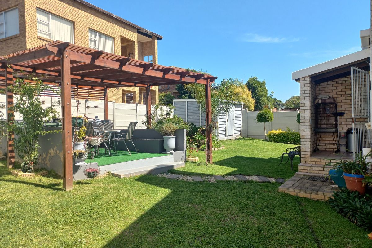 A rear garden featuring a wooden pergola over a raised patio area, a lawn, and a brick structure with a paved entrance.