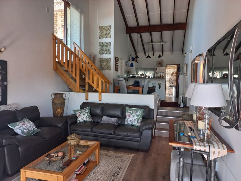 Open-plan living area featuring exposed timber ceiling beams, a split-level layout with a timber staircase, and direct access to the kitchen and dining space.