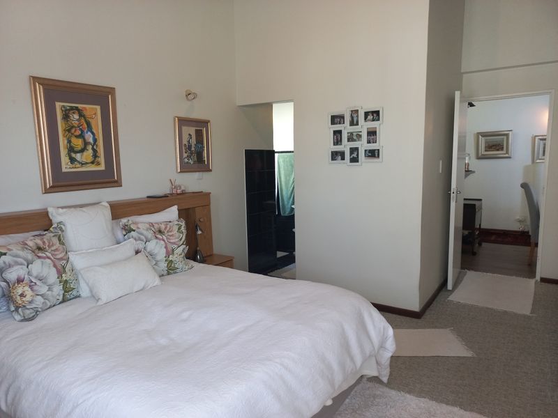 A well-maintained bedroom featuring a built-in headboard, neutral wall finishes, and laminate flooring, with an adjoining en-suite bathroom and hallway access.