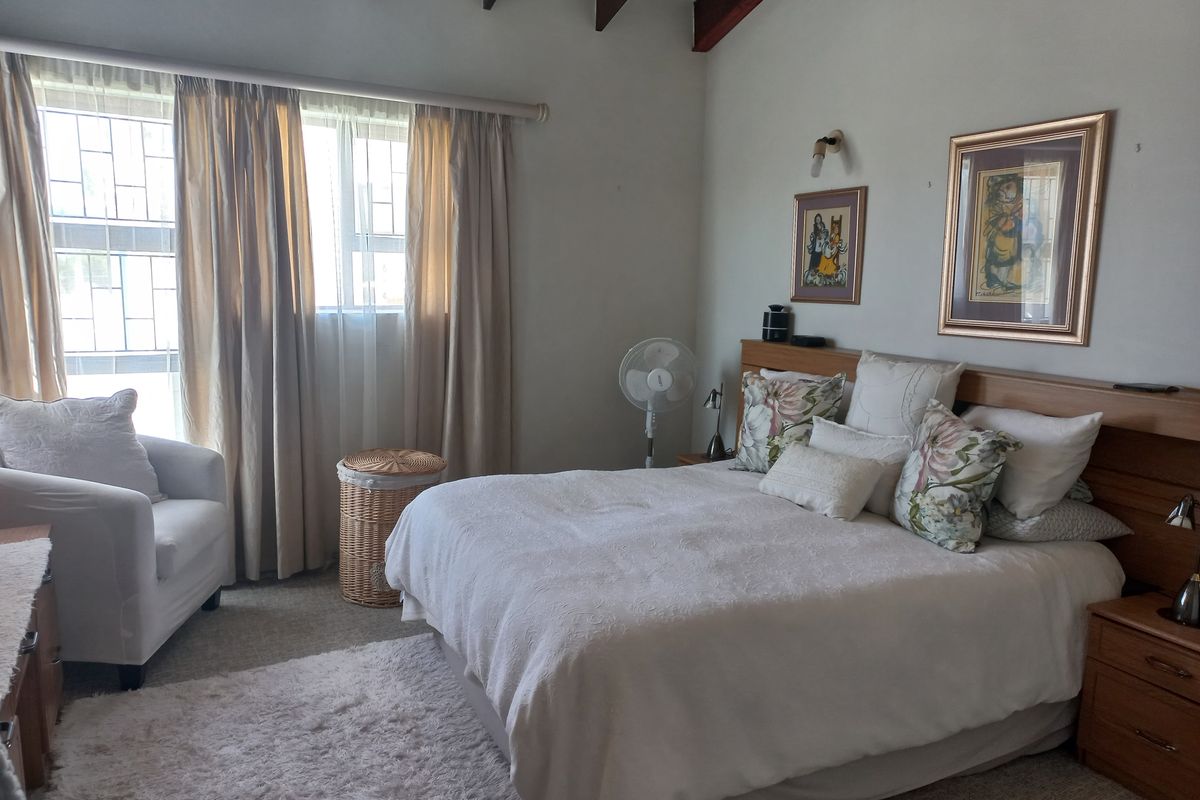 A comfortable bedroom featuring exposed timber ceiling beams, a built-in headboard, and large windows fitted with security bars.