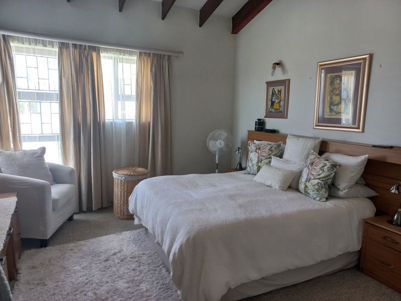 A comfortable bedroom featuring exposed timber ceiling beams, a built-in headboard, and large windows fitted with security bars.
