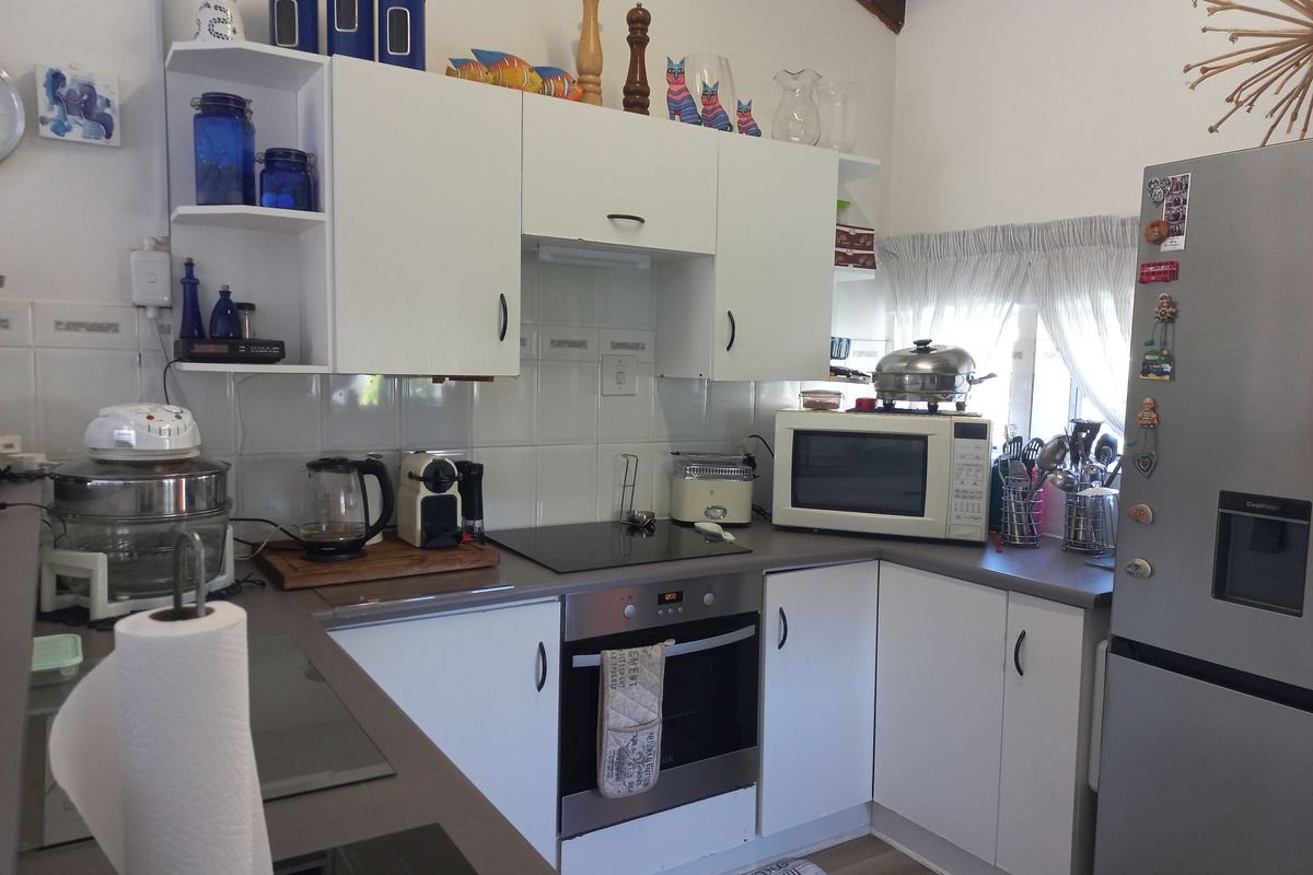 A functional kitchen featuring white cabinetry, a built-in oven with a ceramic hob, and tiled backsplash, offering a practical layout for daily meal preparation.