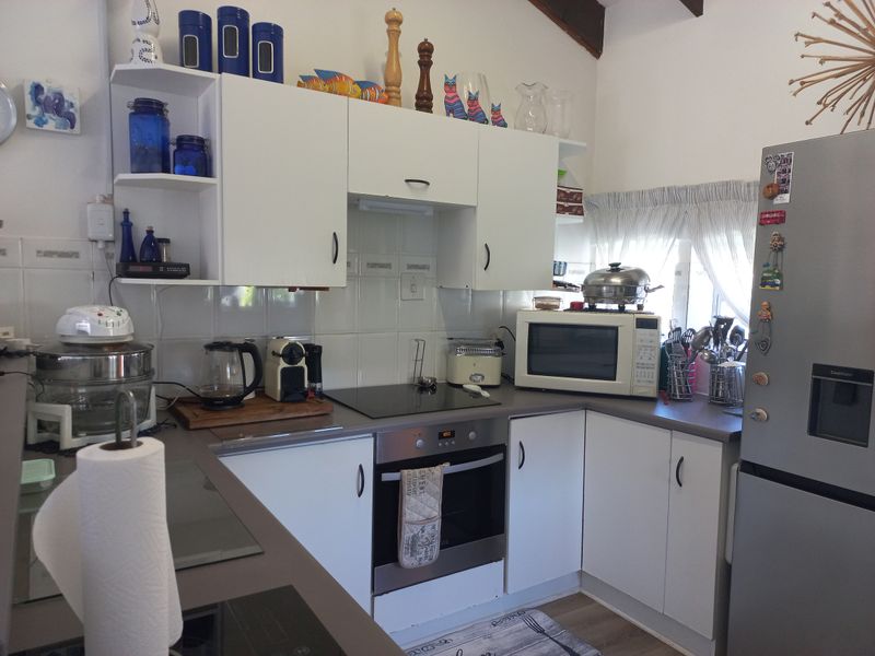 A functional kitchen featuring white cabinetry, a built-in oven with a ceramic hob, and tiled backsplash, offering a practical layout for daily meal preparation.