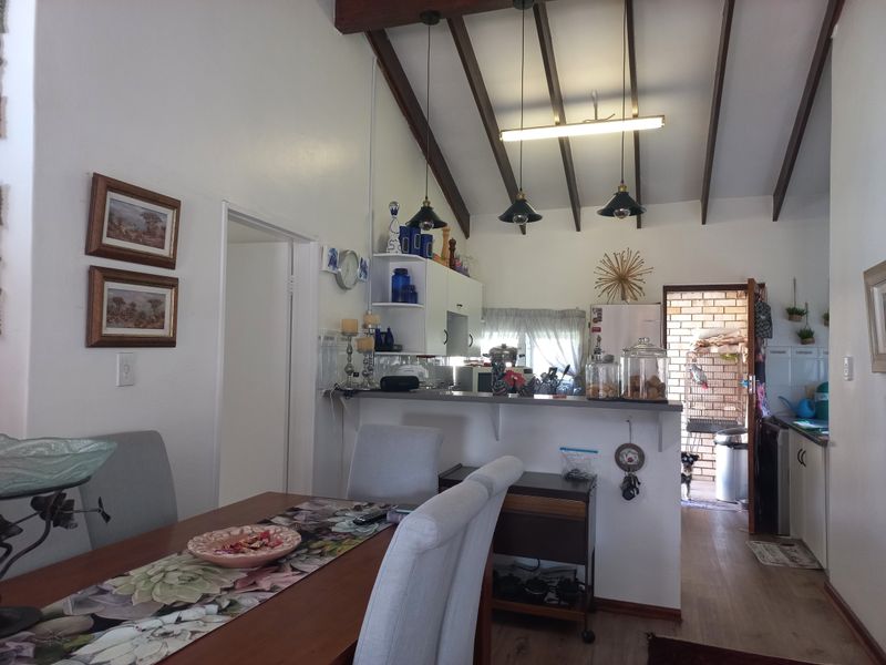 Open plan kitchen and dining area featuring exposed timber ceiling beams, pendant lighting, and a breakfast bar connecting to the kitchen space.