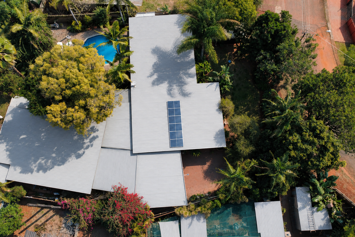 Aerial view of the property showcasing the metal roof with integrated solar panels, a swimming pool, and established garden surroundings.