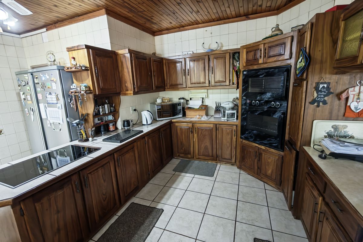 A traditional kitchen featuring extensive wooden cabinetry, a built-in double oven, ceramic hob, tiled splashbacks, and a distinctive timber-clad ceiling.