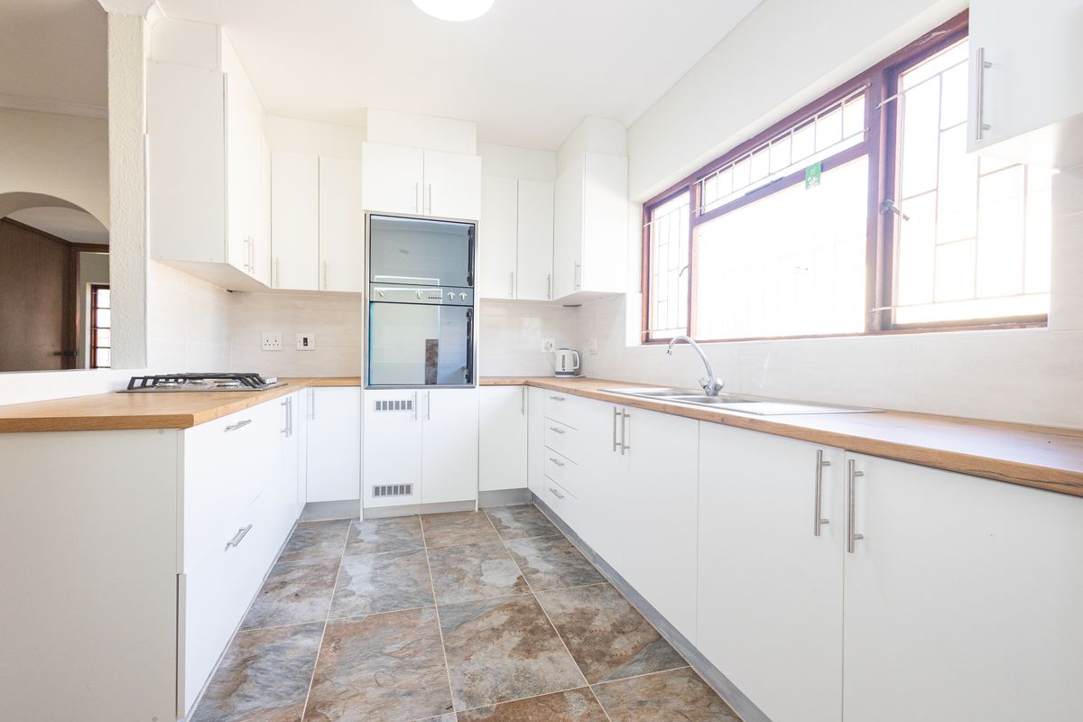 A bright, functional kitchen featuring white cabinetry, wooden countertops, a built-in oven, gas hob, and tiled flooring with a large window.