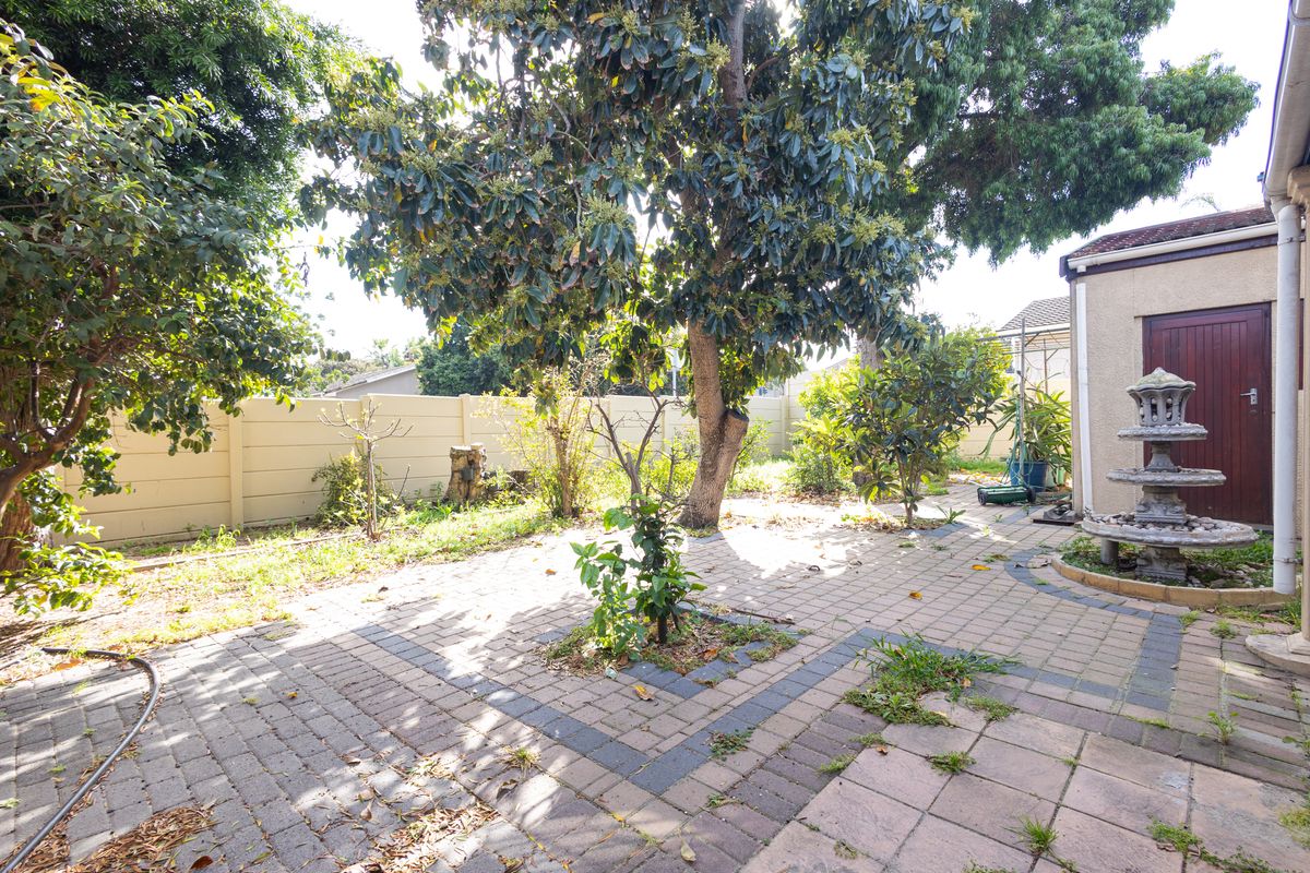 A rear garden area featuring paved patio space, a stone water feature, and established trees, enclosed by a boundary wall.