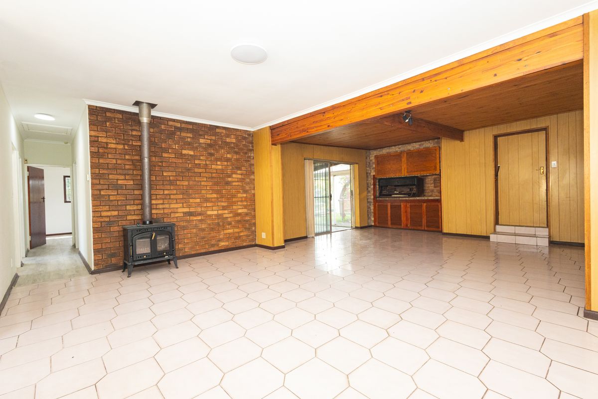 Spacious living area featuring a brick feature wall with a wood-burning stove, timber ceiling beams, and tiled flooring, offering a versatile layout.