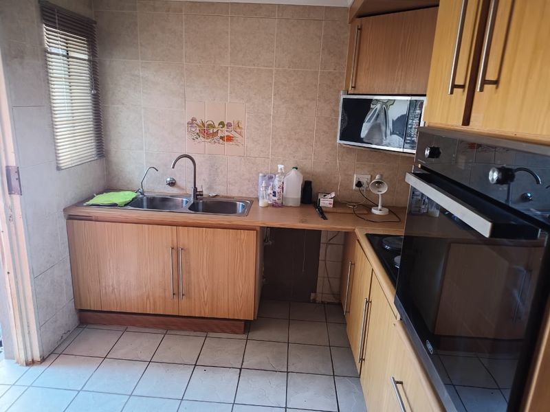 A functional kitchen featuring wood-finish cabinetry, a double sink, built-in oven, and hob, with tiled splashbacks and flooring.