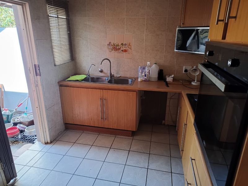Functional scullery area featuring double bowl sink, built-in oven, laminate cabinetry, and tiled flooring with direct access to the exterior.