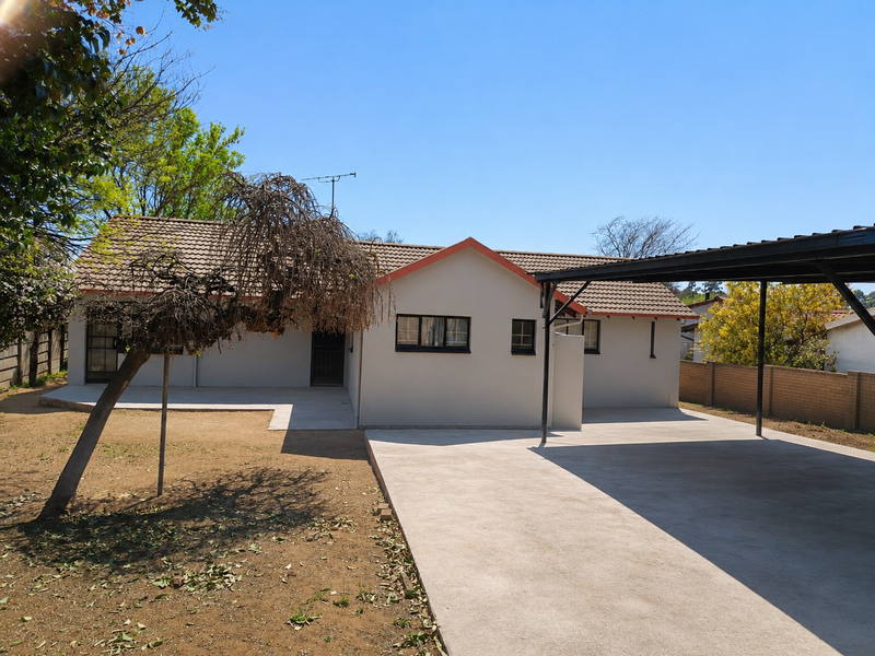 Rear view of the property featuring a concrete driveway, covered carport, tiled roof, and a paved patio area within a fenced yard.